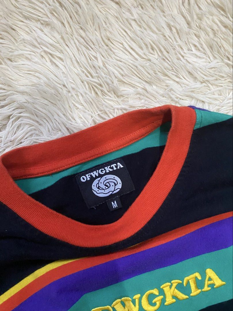 OFWGKTA Striped Long Sleeve Tee (Category: Longsleeves) located in Manila. Submitted by switchcity (Listing ID 1470075818, Image 3). Description: - Brand: OFWGKTA - Style: Long sleeve shirt with horizontal stripes (green, purple, orange, yellow) - Details: Orange ribbed collar and cuffs, embroidered yellow logo on chest, classic donut logo on interior neck tag - Size: Medium - Condition: Clean fabric with bright, vibrant colors.