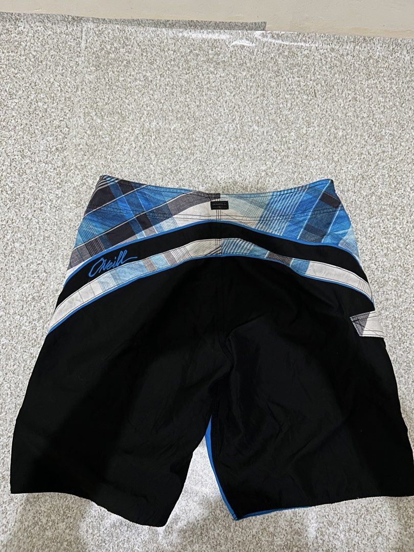 O'Neill Board Shorts Blue Black Plaid (Category: Swim Trunks & Board Shorts) located in Angeles City. Submitted by johngamboa (Listing ID 1469951230, Image 3). Description: - Brand: O'Neill - Style: Classic surf board shorts - Design: Blue, black, and white plaid with vibrant colorblocking - Waist: Drawstring closure with black cords - Pockets: Side pocket with flap and key loop detail - Branding: Embroidered O'Neill script logo on the back and s