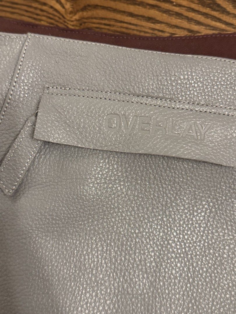OVERLAY rig belt bag in mist (Category: Cross-body Bags) located in Manila. Submitted by oliveginmartini (Listing ID 1470108792, Image 2). Description: - Brand: OVERLAY - Color: Grey - Material: Premium textured leather with embossed logo on front flap - Design: Integrated belt with metal ring hardware - Closure: Secure hook-and-loop on the back strap - Versatility: Functional pouch style, worn around the waist or hips.