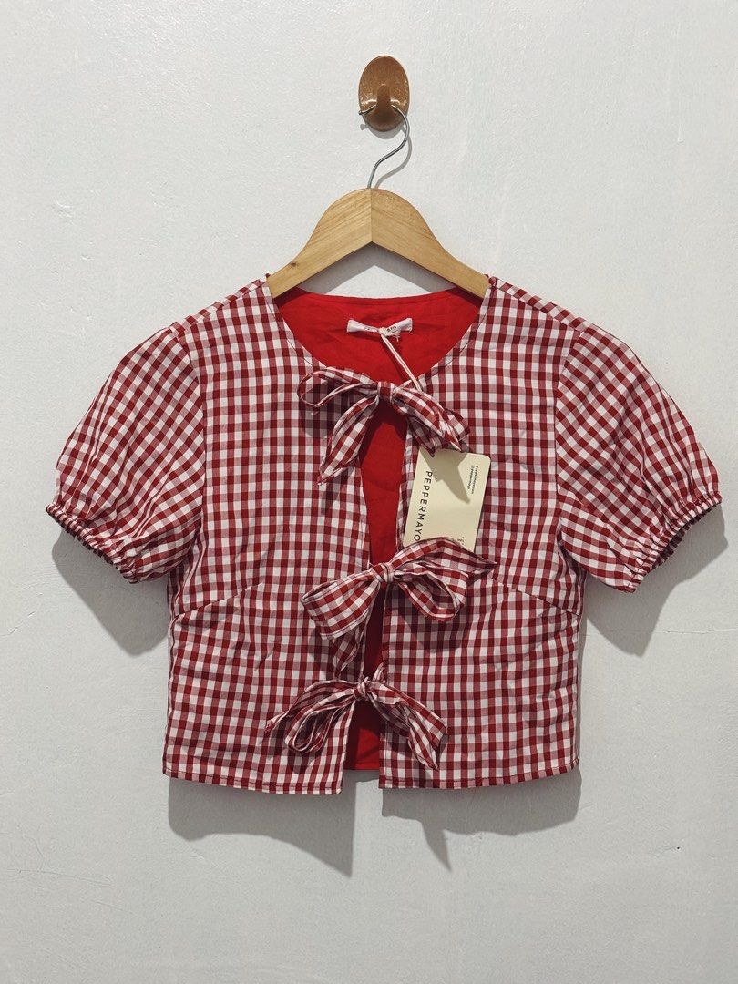 PEPPERMAYO RED GINGHAM BOW TIE CROP TOP (Category: Blouses) located in Angeles City. Submitted by chic.haven (Listing ID 1470039151, Image 1). Description: - Brand: Peppermayo - Style: Red and white gingham crop top - Sleeves: Short puff sleeves with elastic cuffs - Closure: Front opening with three tie bows - Details: Features a contrasting red inner lining - Condition: Brand new with tags still attached.
