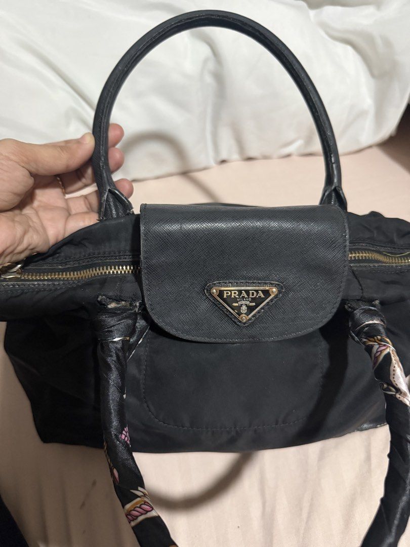Prada Black Nylon Handbag with strap (Category: Luxury Bags & Wallets) located in San Pablo. Submitted by prelovedbymistyblue (Listing ID 1470051678, Image 3). Description: - Prada black nylon handbag - Features iconic metal triangle logo and leather flap pocket - Gold-tone hardware with top zip closure - Includes top handles wrapped in a stylish patterned twilly scarf - Comes with an adjustable black leather shoulder strap - Condition: Minor fab