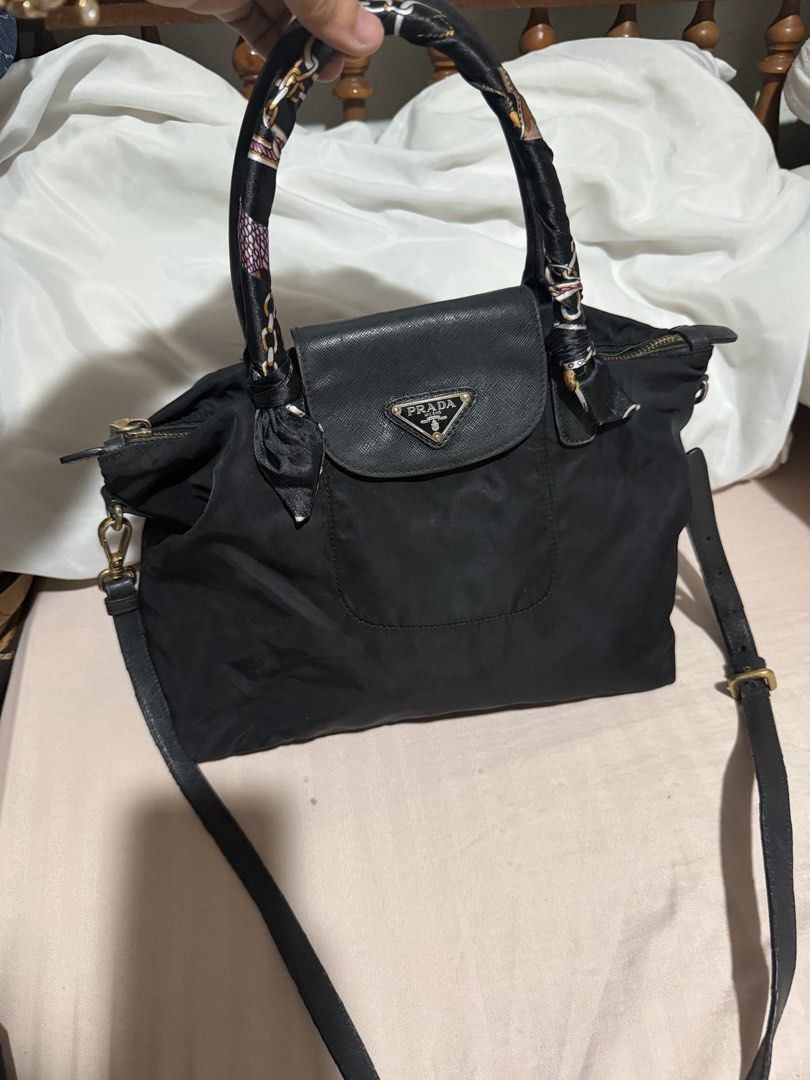 Prada Black Nylon Handbag with strap (Category: Luxury Bags & Wallets) located in San Pablo. Submitted by prelovedbymistyblue (Listing ID 1470051678, Image 1). Description: - Prada black nylon handbag - Features iconic metal triangle logo and leather flap pocket - Gold-tone hardware with top zip closure - Includes top handles wrapped in a stylish patterned twilly scarf - Comes with an adjustable black leather shoulder strap - Condition: Minor fab