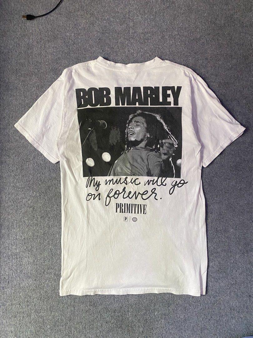 Primitive x Bob Marley White Graphic Tee (Category: Tshirts & Polo Shirts ) located in Maria Aurora. Submitted by mightypenguin.f7ca53 (Listing ID 1470057087, Image 3). Description: White graphic tee from the Primitive and Bob Marley collaboration. Front features Primitive lettering and Bob Marley's signature in gold. Back has a large photo graphic of Bob Marley performing alongside the quote "My music will go on forever." Tagged size and materia