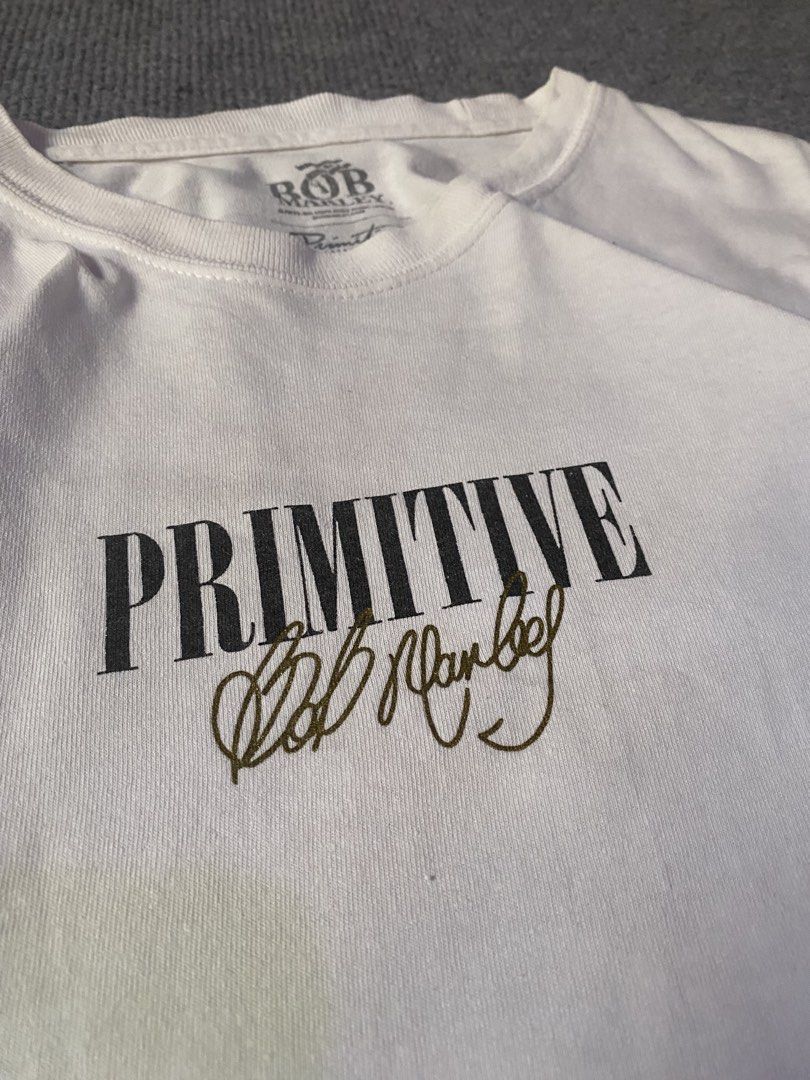 Primitive x Bob Marley White Graphic Tee (Category: Tshirts & Polo Shirts ) located in Maria Aurora. Submitted by mightypenguin.f7ca53 (Listing ID 1470057087, Image 2). Description: White graphic tee from the Primitive and Bob Marley collaboration. Front features Primitive lettering and Bob Marley's signature in gold. Back has a large photo graphic of Bob Marley performing alongside the quote "My music will go on forever." Tagged size and materia