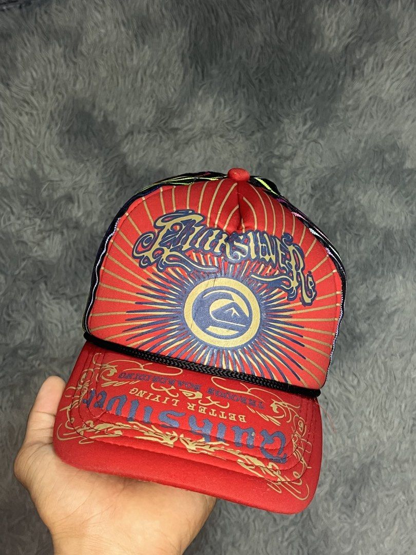 Quiksilver Red Graphic Trucker Cap with Multi-color Mesh (Category: Caps & Hats) located in Muntinlupa City. Submitted by pastforwardthrift (Listing ID 1470125873, Image 1). Description: - Brand: Quiksilver - Color: Red with black mesh back - Design: Large front graphic logo with sunburst artwork and colourful vertical stripes on the back - Closure: Adjustable snapback - Condition: Clean brim, structured front panels, and interior tag intact.