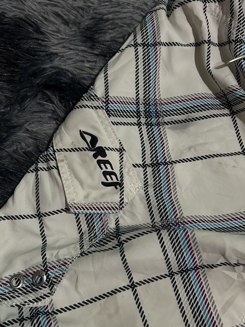 Reef Plaid Board Shorts Packable Size 31 W15 L21 (Category: Swim Trunks & Board Shorts) located in Cadiz. Submitted by jaybatiller (Listing ID 1470051548, Image 2). Description: - Brand: Reef - Style: Board shorts in white plaid with blue and purple stripes - Size: 31 waist - Material: 100% quick-dry polyester - Features: Front drawstring closure, right-leg cargo pocket with Reef logo, and small hem tag - Care: Hand wash only - Condition: Ready f