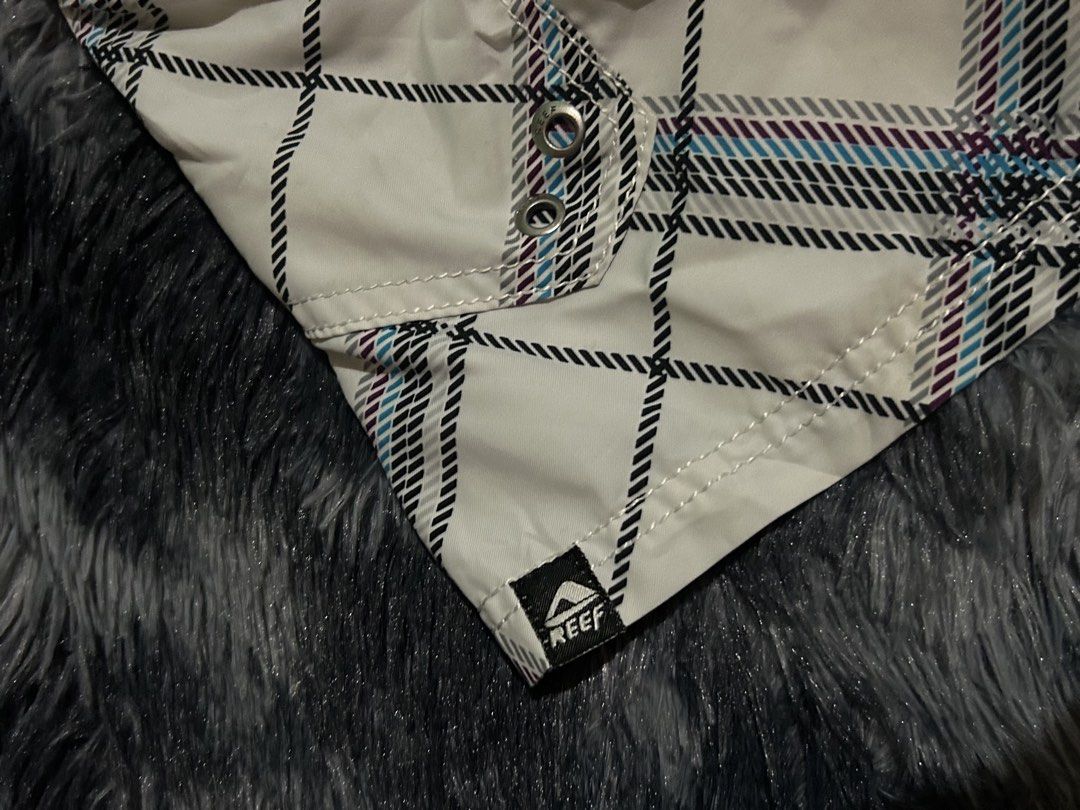 Reef Plaid Board Shorts Packable Size 31 W15 L21 (Category: Swim Trunks & Board Shorts) located in Cadiz. Submitted by jaybatiller (Listing ID 1470051548, Image 3). Description: - Brand: Reef - Style: Board shorts in white plaid with blue and purple stripes - Size: 31 waist - Material: 100% quick-dry polyester - Features: Front drawstring closure, right-leg cargo pocket with Reef logo, and small hem tag - Care: Hand wash only - Condition: Ready f