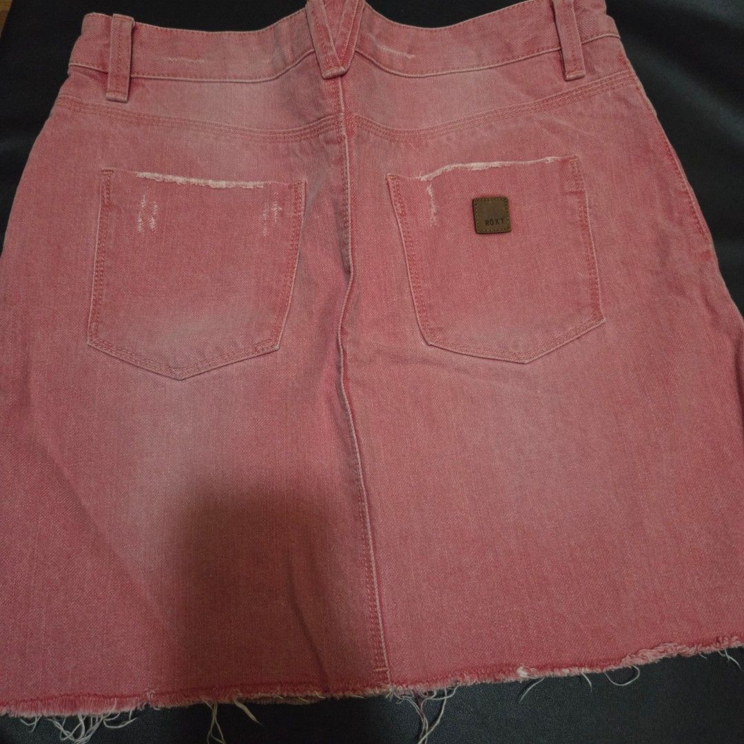 Roxy Pink Denim Skirt Size 12 (Category: Skirts) located in Makati City. Submitted by lexshie (Listing ID 1469977890, Image 3). Description: - Brand/Style: Roxy denim skirt in a trendy washed pink - Size: 12 (tagged on waistband) - Design details: Raw frayed hemline with slight distressing on the pockets - Features: Classic five-pocket styling, zipper fly, and button closure - Accents: Small Roxy leather patch on the back pocket - Condition/Vibe: