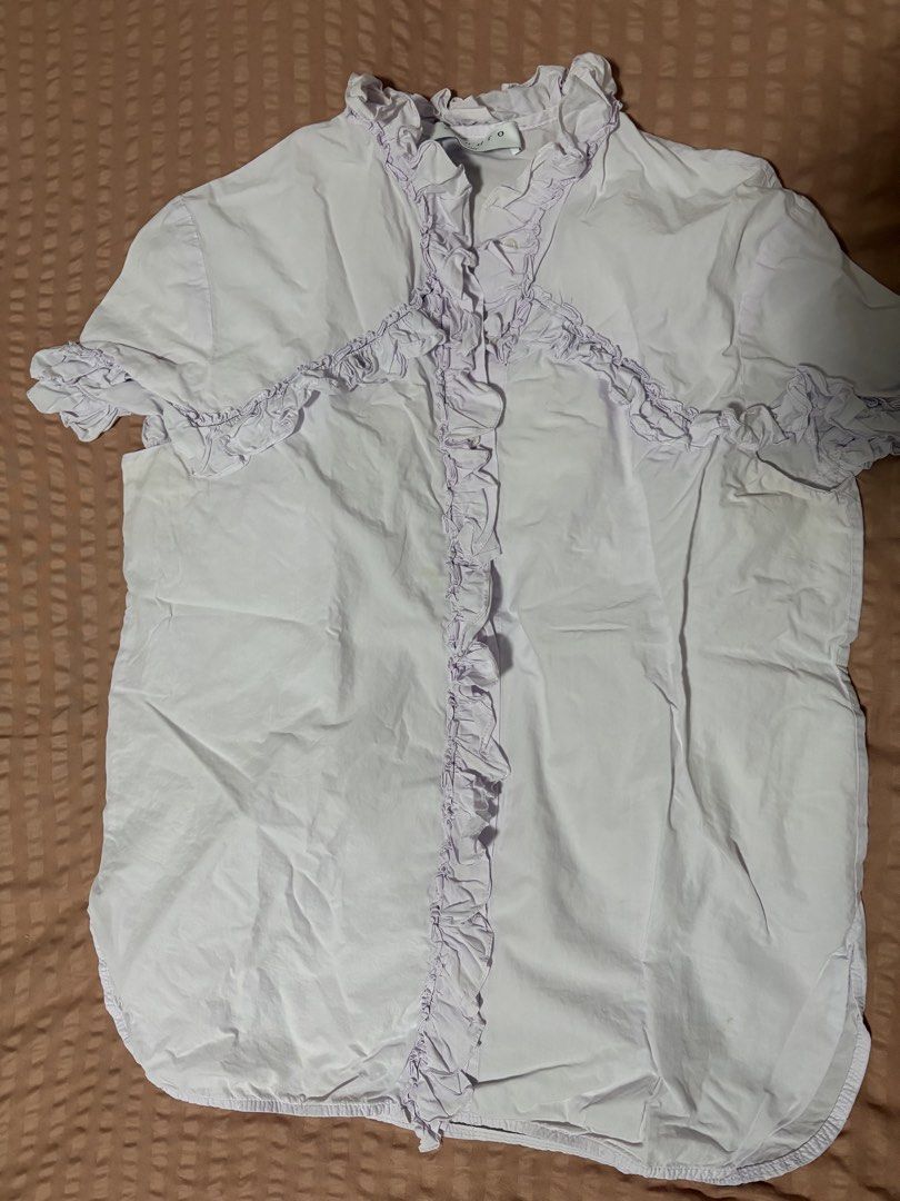 Sandro Paris Ruffled Short Sleeve Lavender Blouse (Category: Blouses) located in Quezon City. Submitted by bluefrenchorn (Listing ID 1470068280, Image 2). Description: - Brand: Sandro Paris - Color: Soft pastel lavender - Features: Ruffles along the front placket, collar, high neck, and short sleeves with a button-up front - Measurements: Pit-to-pit ~18.5 inches, Length ~23.5 inches - Condition: Gentle wear with a minor spot near the bottom hem -