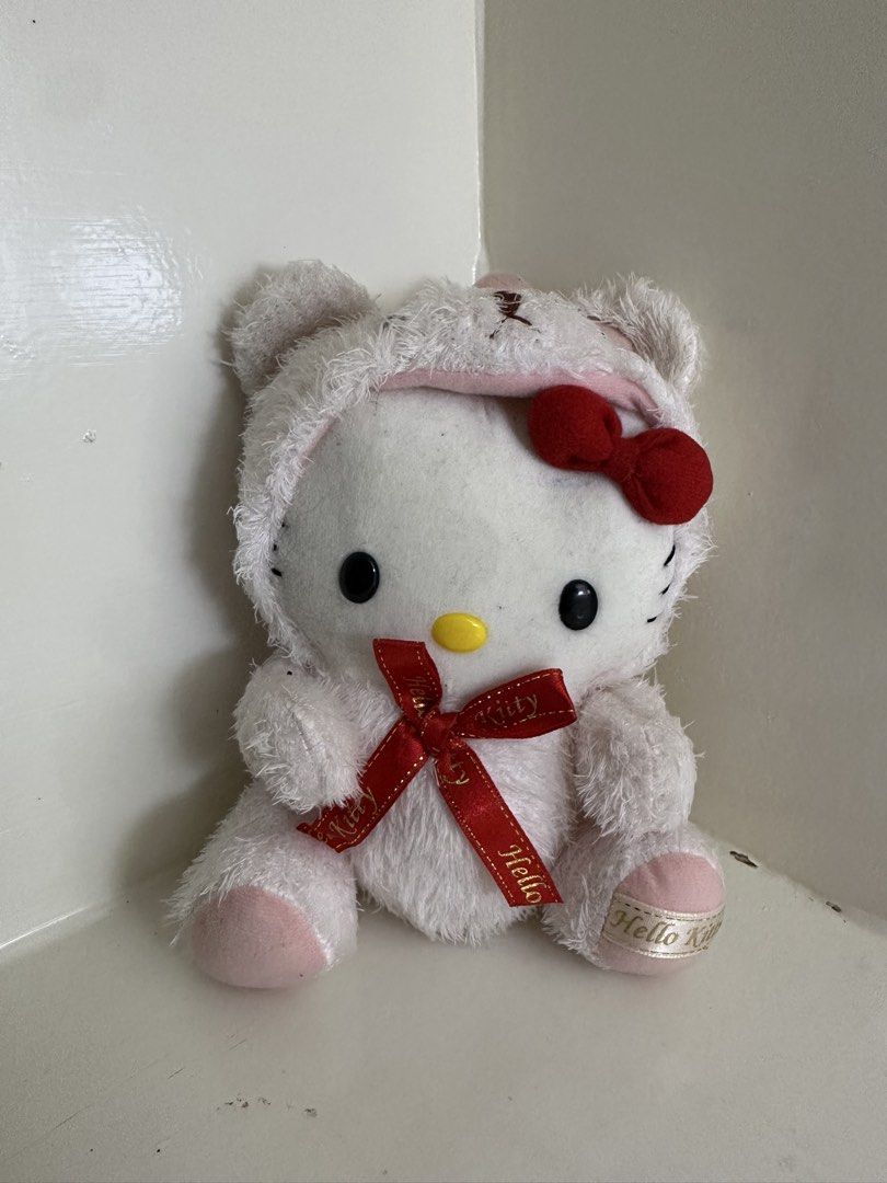 Sanrio Hello Kitty Bear Plush Toy 2002 (Category: Plushies & Soft Toys) located in Quezon City. Submitted by swift.thriftz (Listing ID 1470121471, Image 1). Description: - Official Sanrio Kitty plush toy with 1976/2002 license - Adorable design dressed in a fuzzy white bear hoodie with pink accents - Features a red bow on the hood and a larger red ribbon with Kitty lettering around the neck - Cute pink paws detailed with golden Kitty text ribbon.
