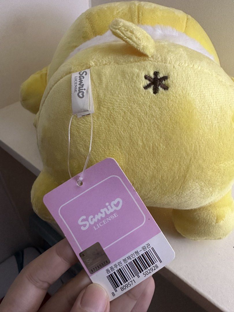 Sanrio Pompompurin Crown Plush Toy (Category: Plushies & Soft Toys) located in Quezon City. Submitted by swift.thriftz (Listing ID 1470121461, Image 2). Description: - Authentic Sanrio Pompompurin plushie with original tag (barcode and holographic sticker included) - Made with ultra-soft golden yellow fabric featuring embroidered facial features and a cute brown tail - Adorned with a yellow and white striped crown - Wears a large satin yellow rib