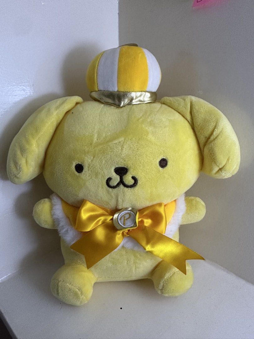 Sanrio Pompompurin Crown Plush Toy (Category: Plushies & Soft Toys) located in Quezon City. Submitted by swift.thriftz (Listing ID 1470121461, Image 1). Description: - Authentic Sanrio Pompompurin plushie with original tag (barcode and holographic sticker included) - Made with ultra-soft golden yellow fabric featuring embroidered facial features and a cute brown tail - Adorned with a yellow and white striped crown - Wears a large satin yellow rib