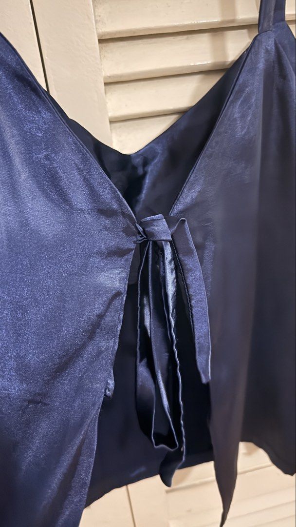 [Self-Tie Back] Navy Blue Satin V-Neck Tie-Back Cami Top (Category: Sleeveless) located in Quezon City. Submitted by oliviablanche (Listing ID 1470112850, Image 2). Description: - Size: Free size - Color: Navy Blue - Neckline: Soft V-neckline with thin shoulder straps a Details: Smooth satin-like fabric with a subtle sheen, relaxed silhouette, straight hem, and self-tie bow detail at the back - Styling: Versatile and elegant, easy to dress up wit