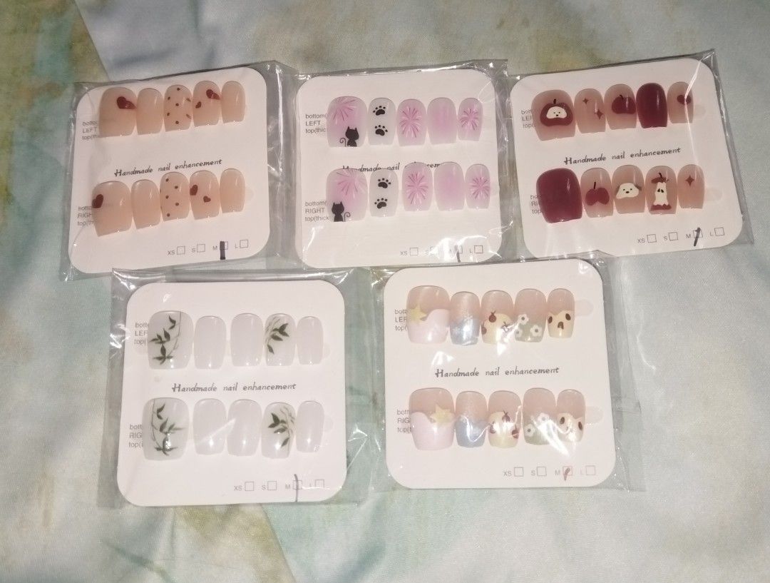 Handmade press-on nail sets - assorted cute designs (Category: Hands & Nails) located in Caloocan City. Submitted by ltriciamae (Listing ID 1469960452, Image 1). Description: 5 DESIGNS SET — ₱100 ONLY TAKE ALL!! - Handcrafted press-on nail enhancements - Short square shape across all 5 styles - Fun designs: red hearts, black cats, green bamboo leaves, and apple dogs - Each set comes sealed on a display card with size indicators - Available per se