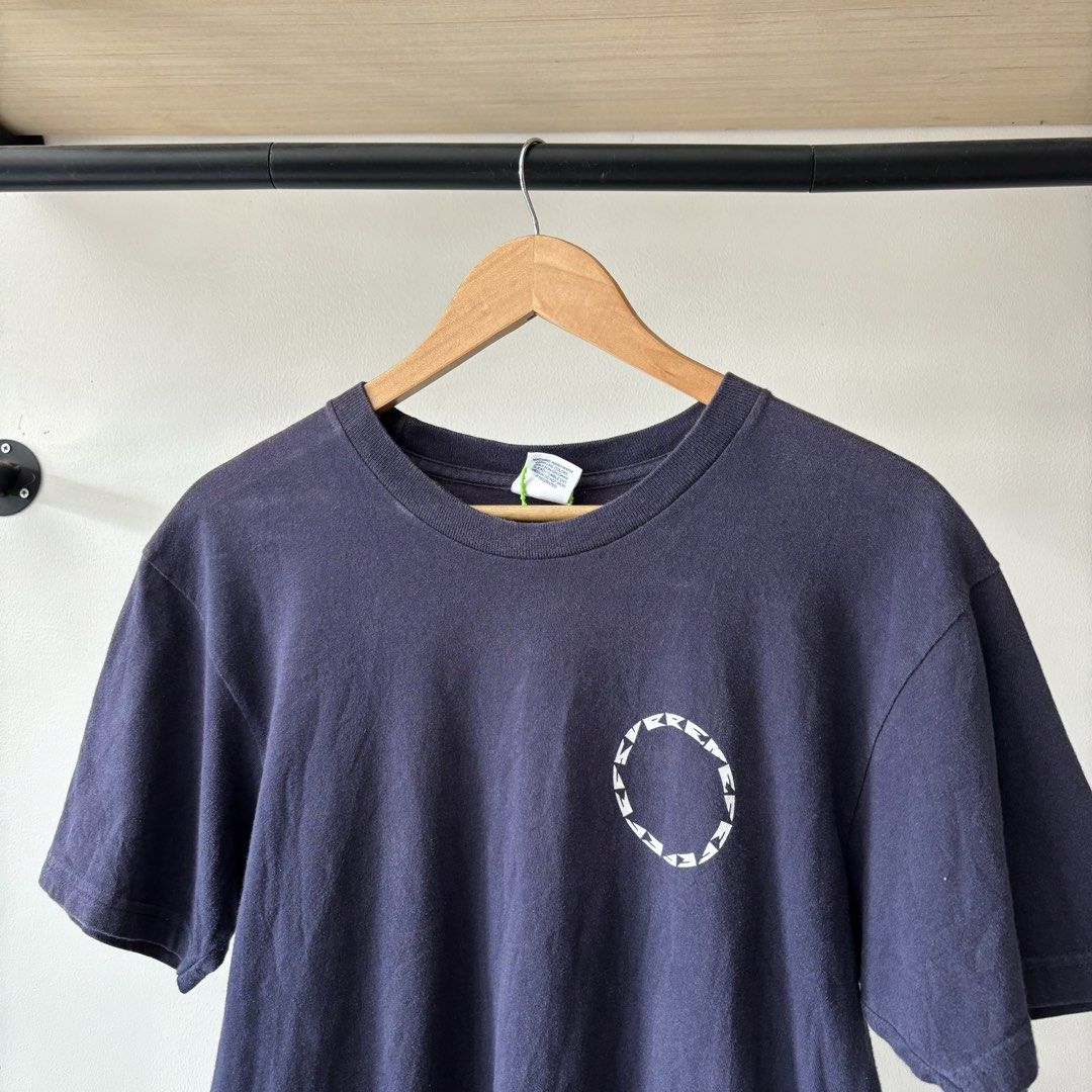 Supreme Navy Graphic T-Shirt Medium (Category: Tshirts & Polo Shirts ) located in Bambang. Submitted by heats777 (Listing ID 1470018760, Image 1). Description: - Brand: Supreme - Color: Navy blue (slightly faded, lived-in look) - Size: Medium - Material: Pre-shrunk cotton - Design: Small circular graphic on front left chest; large face graphic inside a pink circular text frame on the back - Condition: Used.