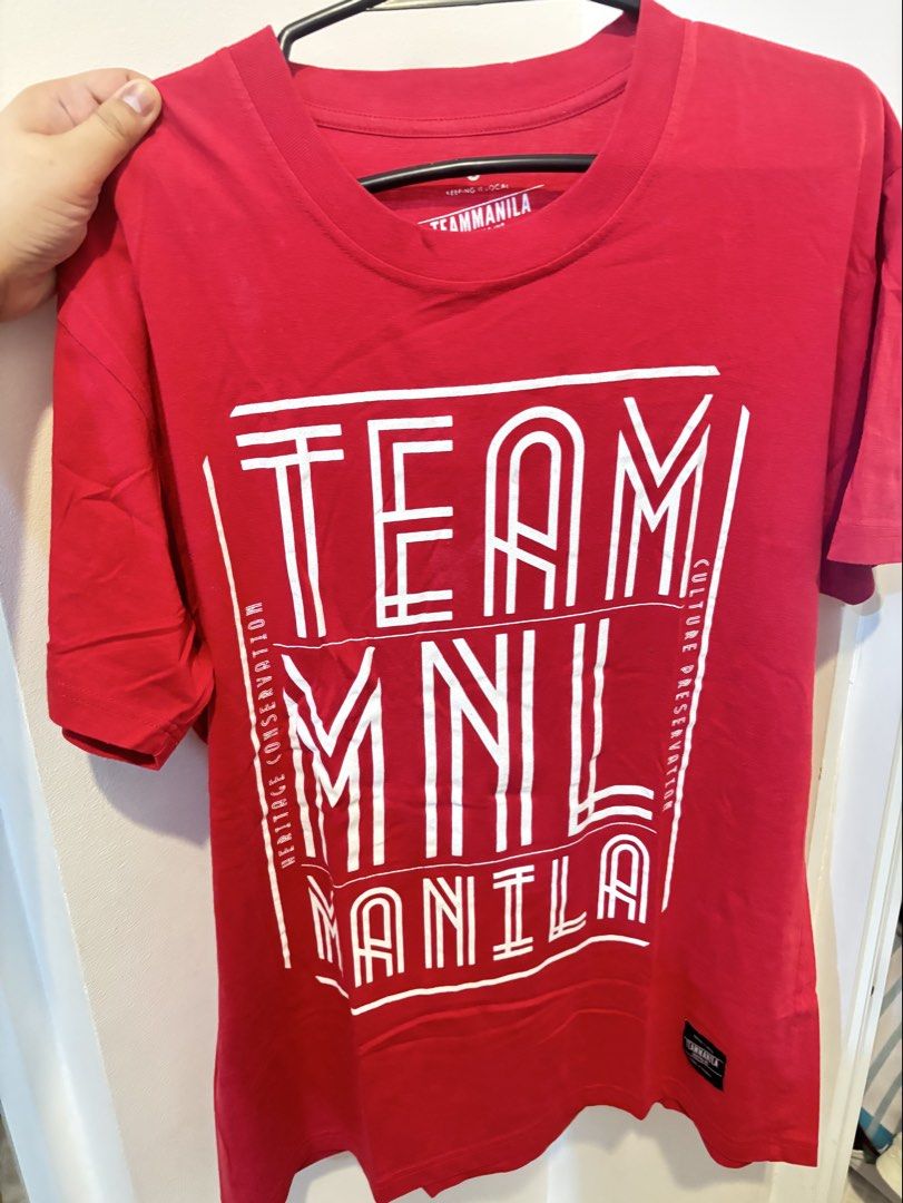 Team Manila Red Graphic T-Shirt (Category: Tshirts & Polo Shirts ) located in Navotas City. Submitted by psgvv (Listing ID 1470090849, Image 1). Description: - Brand: Team Manila - Color: Vibrant red - Size: L (tagged on inner collar) - Design: White block text print with border lines and side details on chest - Details: Crew neckline, short sleeves, and woven fabric label near bottom hem - Back: Clean, solid red.