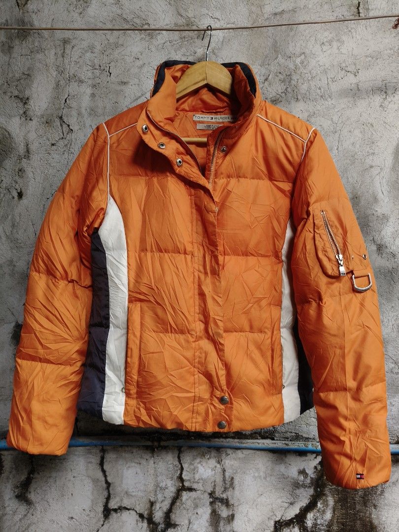 Tommy Hilfiger Orange Puffer Jacket (Category: Coats, Jackets and Outerwear) located in Makati City. Submitted by thriftersmakati (Listing ID 1470062809, Image 1). Description: - Brand: Tommy Hilfiger - Size: XS - Color: Bright orange with white and dark side panels - Details: Zipper pocket and metal D-ring on the left sleeve - Branding: Iconic embroidered flag logo on cuff and sleeve - Comfort: Ribbed inner cuffs to lock in warmth - Closure: Hea