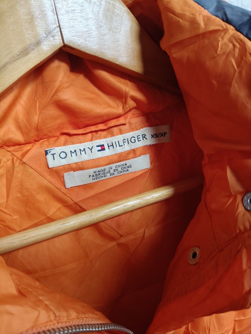 Tommy Hilfiger Orange Puffer Jacket (Category: Coats, Jackets and Outerwear) located in Makati City. Submitted by thriftersmakati (Listing ID 1470062809, Image 2). Description: - Brand: Tommy Hilfiger - Size: XS - Color: Bright orange with white and dark side panels - Details: Zipper pocket and metal D-ring on the left sleeve - Branding: Iconic embroidered flag logo on cuff and sleeve - Comfort: Ribbed inner cuffs to lock in warmth - Closure: Hea