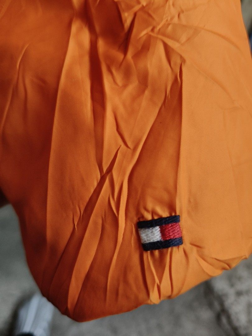 Tommy Hilfiger Orange Puffer Jacket (Category: Coats, Jackets and Outerwear) located in Makati City. Submitted by thriftersmakati (Listing ID 1470062809, Image 3). Description: - Brand: Tommy Hilfiger - Size: XS - Color: Bright orange with white and dark side panels - Details: Zipper pocket and metal D-ring on the left sleeve - Branding: Iconic embroidered flag logo on cuff and sleeve - Comfort: Ribbed inner cuffs to lock in warmth - Closure: Hea