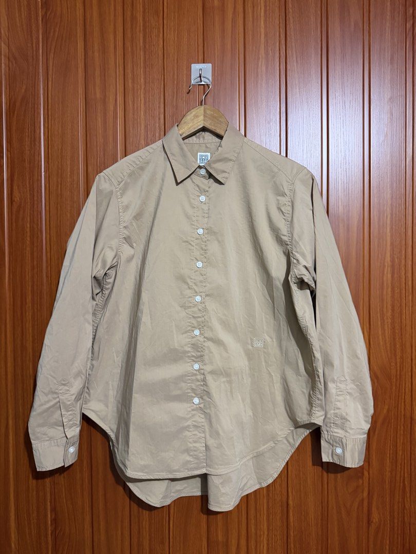 TOTEME Beige Long Sleeve Button-Down Shirt (Category: Longsleeves) located in Manila. Submitted by tlfph (Listing ID 1470109226, Image 1). Description: - Brand: Toteme - Color: Classic beige - Fit: Relaxed fit with a curved hemline - Details: Pointed collar, button cuffs, and subtle embroidered monogram at the hem - Styling: Versatile; pairs well with both denim and tailored pants - Note: Measurements available upon request.