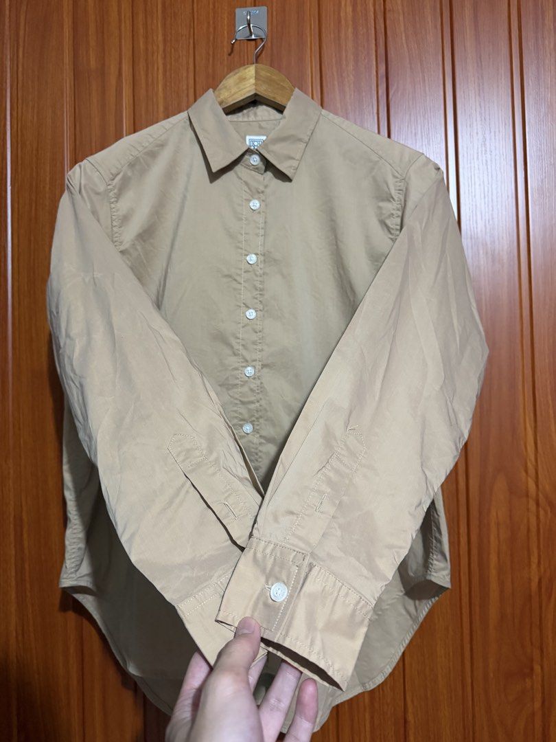 TOTEME Beige Long Sleeve Button-Down Shirt (Category: Longsleeves) located in Manila. Submitted by tlfph (Listing ID 1470109226, Image 3). Description: - Brand: Toteme - Color: Classic beige - Fit: Relaxed fit with a curved hemline - Details: Pointed collar, button cuffs, and subtle embroidered monogram at the hem - Styling: Versatile; pairs well with both denim and tailored pants - Note: Measurements available upon request.