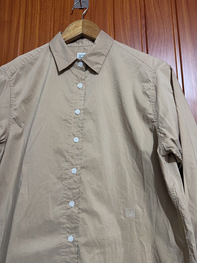 TOTEME Beige Long Sleeve Button-Down Shirt (Category: Longsleeves) located in Manila. Submitted by tlfph (Listing ID 1470109226, Image 2). Description: - Brand: Toteme - Color: Classic beige - Fit: Relaxed fit with a curved hemline - Details: Pointed collar, button cuffs, and subtle embroidered monogram at the hem - Styling: Versatile; pairs well with both denim and tailored pants - Note: Measurements available upon request.