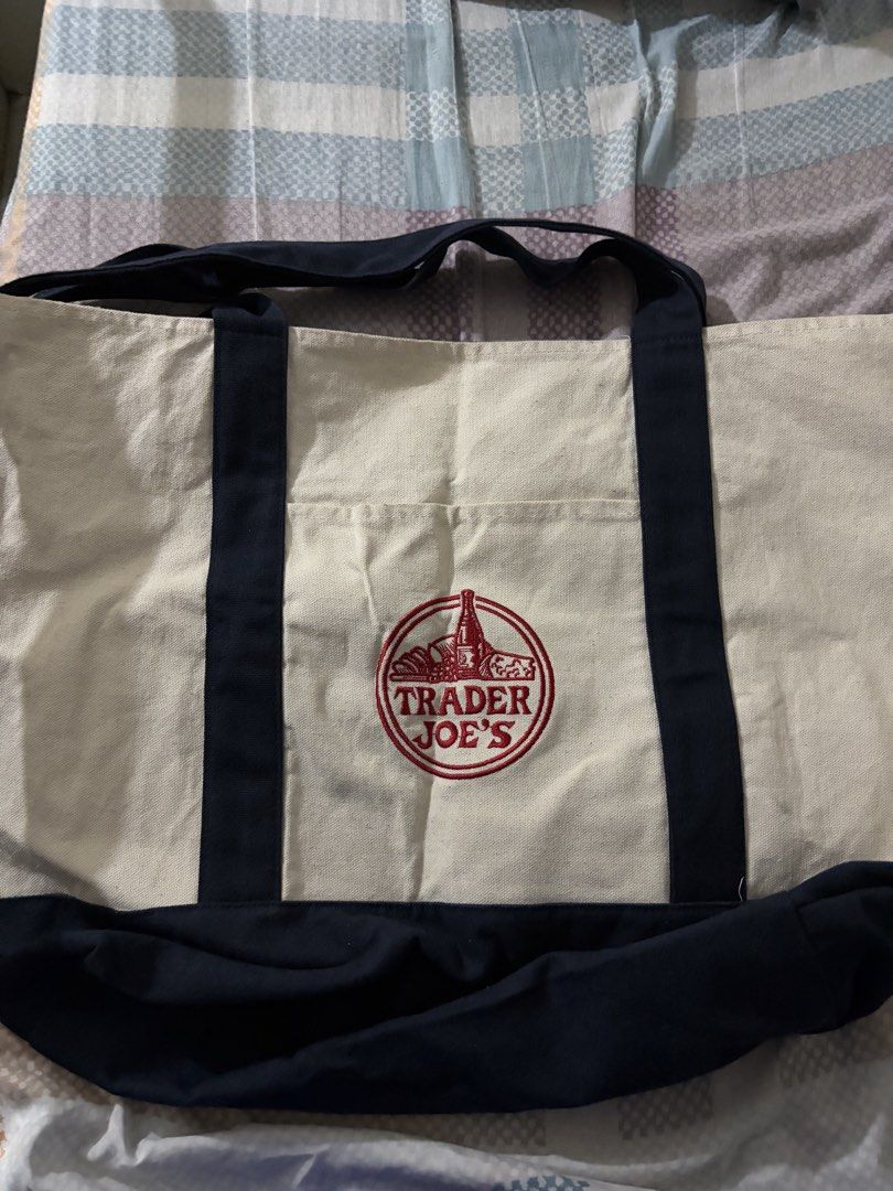 Trader Joe's Canvas Tote Bag (Original) (Category: Tote Bags) located in Manila. Submitted by lestcalderon (Listing ID 1470091222, Image 1). Description: - Authentic Trader Joe's canvas tote bag - Cream body with dark blue bottom and matching straps - Features a striking red embroidered logo on the front pocket - Made from heavy-duty, durable cotton canvas - Spacious size ideal for grocery runs or everyday carry - Clean interior and exterior, rea