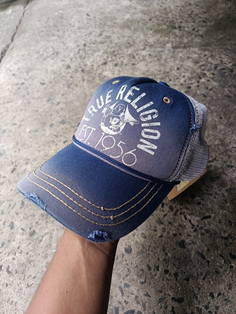True Religion Trucker Cap Blue Distressed Est 1956 (Category: Caps & Hats) located in Caloocan City. Submitted by gemfinder669 (Listing ID 1470000931, Image 2). Description: True Religion trucker cap in blue and white mesh. Distressed details on the brim and crown. Large True Religion logo graphic printed across the front with Est. 1956 lettering. Contrast stitching throughout in orange. Adjustable strap in the back with metal buckle featuring th