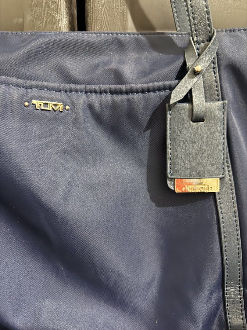 Tumi Blue Nylon Tote Bag with Gold Hardware (Category: Tote Bags) located in Rizal. Submitted by lovegclothingph (Listing ID 1470080307, Image 2). Description: - Brand: Tumi - Material: Navy blue nylon with leather handles and luggage tag - Hardware: Gold-tone logo lettering, zipper closure, and Tumi pull - Interior: Light beige fabric lining - Design: Clean, structured body with double shoulder straps - Condition: Minor wear spots visible near t