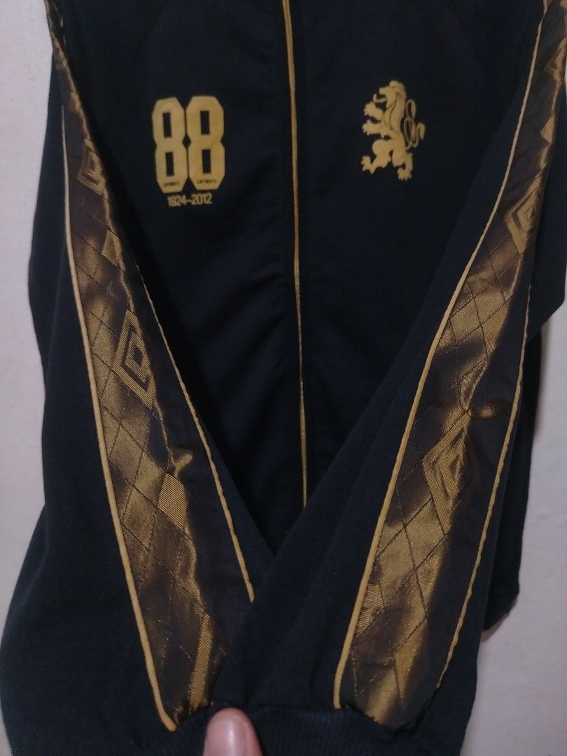 Umbro Black and Gold Track Jacket 1924-2012 (Category: Coats, Jackets and Outerwear) located in Rizal. Submitted by gmpastoffi75031 (Listing ID 1470017681, Image 2). Description: - Brand: Umbro - dimes 21x27.5 - Color: Black with gold trim and gold zipper - Graphics: Number 88 with 1924-2012 on right chest, lion crest on left chest - Details: Small embroidered Umbro diamond logo near hem and patterned taping down both sleeves - Interior: Golden l