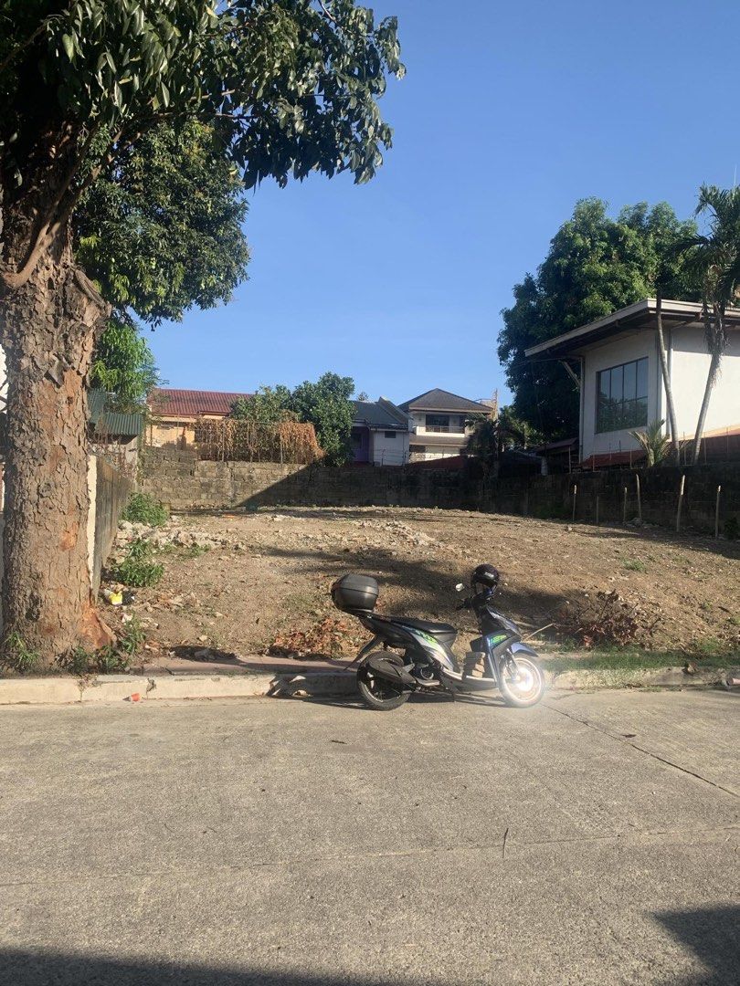 Vacant residential lot ready for building (Category: Lot) located in Manila. Submitted by iamjuliewoo (Listing ID 1470100326, Image 1). Description: - Ready for construction - Cleared and flat terrain - Facing a paved concrete road - Boundary wall already installed at the back - Located in a quiet residential neighborhood with established houses - Features a big mature tree on the left side for natural shade.