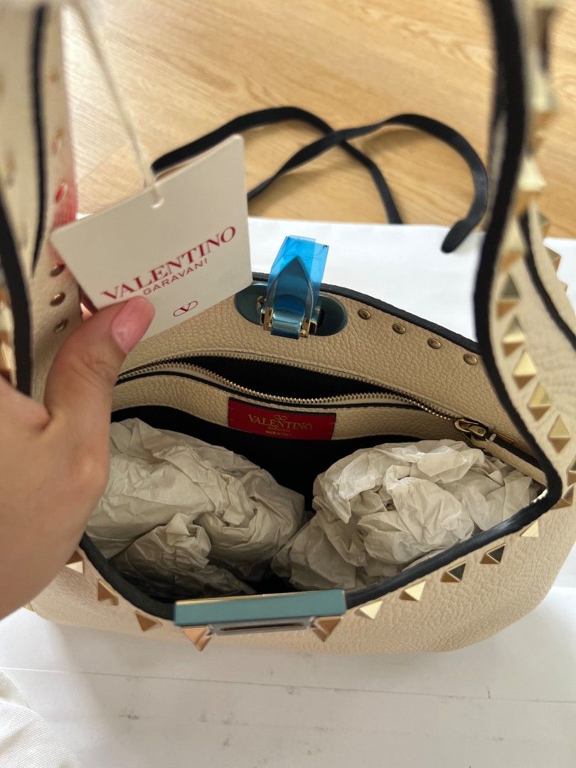 Valentino Garavani Rockstud Shoulder Bag Ivory (Category: Luxury Bags & Wallets) located in Manila. Submitted by vi_ka (Listing ID 1469953065, Image 3). Description: - Brand: Valentino Garavani - Material & Color: Ivory leather with striking gold-tone pyramid studs - Closure: Flap closure with clasp (protective blue plastic still on) - Interior: Vibrant red lining with a zippered pocket and brand logo patch - Condition: Brand new with tag attache