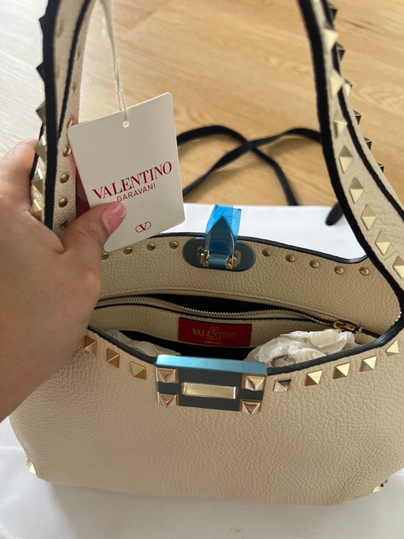 Valentino Garavani Rockstud Shoulder Bag Ivory (Category: Luxury Bags & Wallets) located in Manila. Submitted by vi_ka (Listing ID 1469953065, Image 2). Description: - Brand: Valentino Garavani - Material & Color: Ivory leather with striking gold-tone pyramid studs - Closure: Flap closure with clasp (protective blue plastic still on) - Interior: Vibrant red lining with a zippered pocket and brand logo patch - Condition: Brand new with tag attache