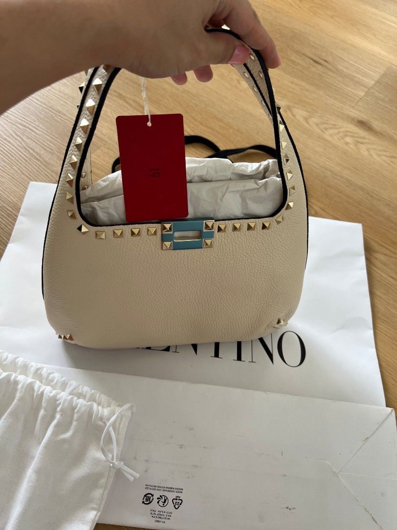 Valentino Garavani Rockstud Shoulder Bag Ivory (Category: Luxury Bags & Wallets) located in Manila. Submitted by vi_ka (Listing ID 1469953065, Image 1). Description: - Brand: Valentino Garavani - Material & Color: Ivory leather with striking gold-tone pyramid studs - Closure: Flap closure with clasp (protective blue plastic still on) - Interior: Vibrant red lining with a zippered pocket and brand logo patch - Condition: Brand new with tag attache