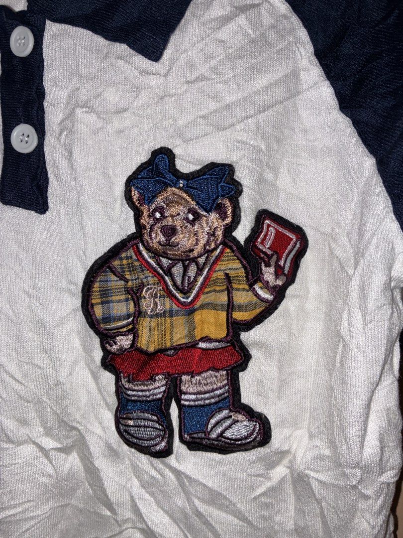 White and Navy Polo Shirt with Bear Patch (Category: Blouses) located in Placer. Submitted by talaalond61563 (Listing ID 1470137386, Image 2). Description: - White short sleeve polo shirt with dark navy raglan sleeves - Features a large embroidered teddy bear patch on the chest - Classic collar with a 2-white-button placket - Stylish white stripe details on the sleeve cuffs - Made from soft, comfortable knit fabric - Perfect for casual wear and e