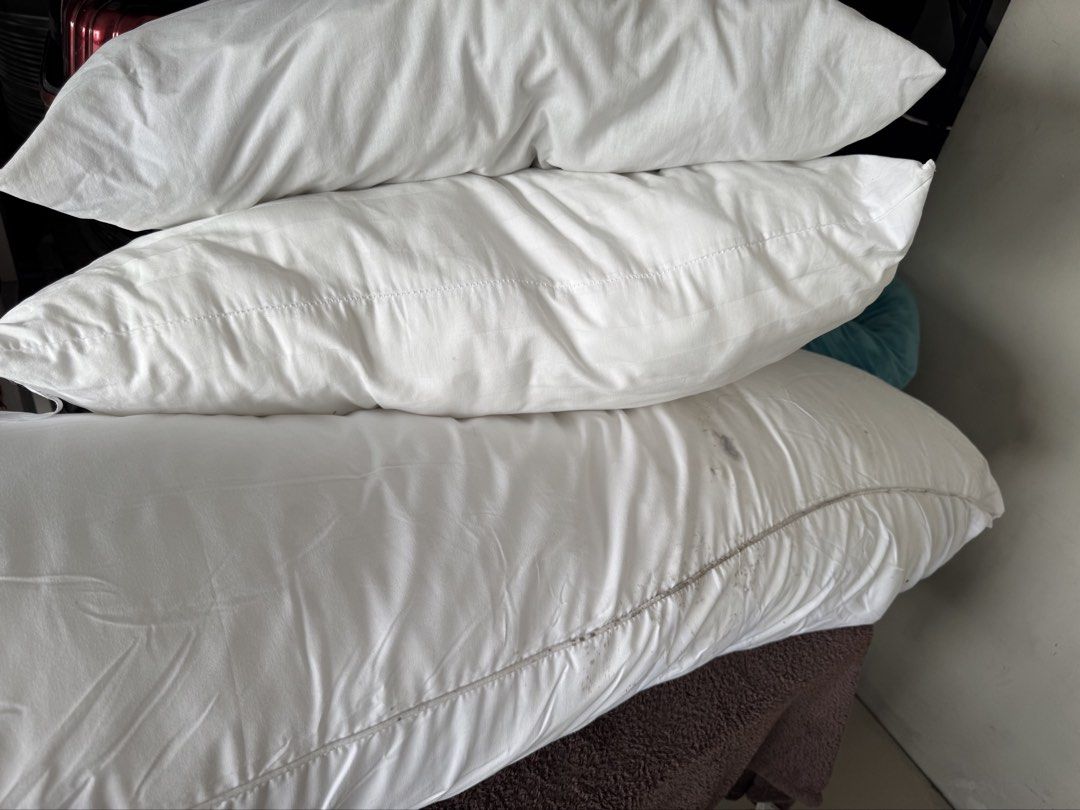 White bed pillows stack of three (Category: Bedding & Towels) located in Manila. Submitted by decluterthings888 (Listing ID 1469966032, Image 1). Description: - Set of 3 white pillows: two standard rectangular pillows and one long bolster style pillow - Clean white cotton covers overall - Flaw: Noticeable dark stains along the seam and surface of the bottom bolster pillow - Ideal for spare guest beds, outdoor lounging, or repurposing with new pil