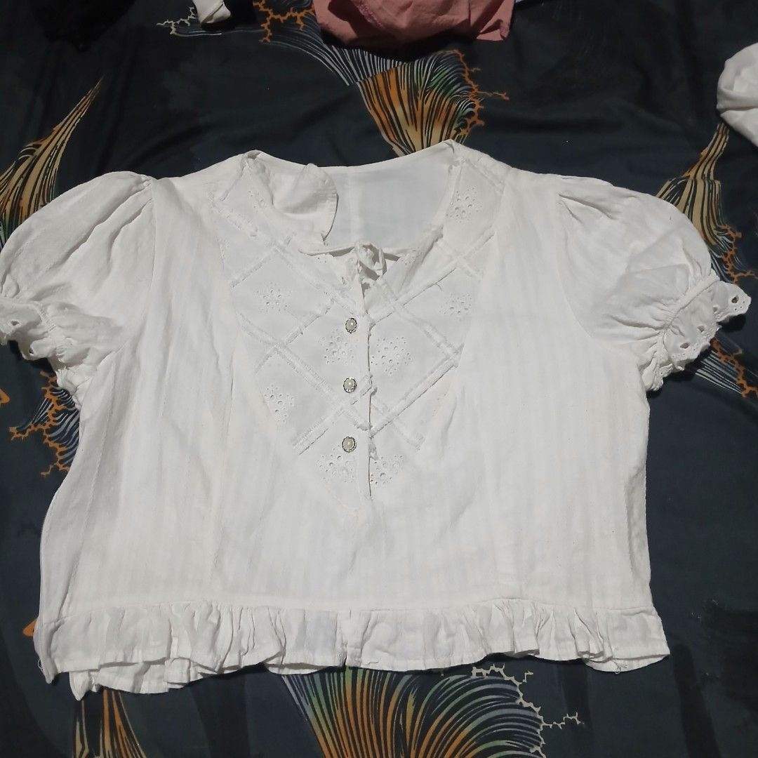 White Short Sleeve Blouse with Ruffled Hem (Category: Blouses) located in Manila. Submitted by iiselou (Listing ID 1470102110, Image 1). Description: - Color: White - Material: Lightweight cotton - Design: Eyelet embroidery panels on the front - Sleeves: Short puffed sleeves with ruffled cuffs - Details: Three decorative chest buttons, neckline tie detail, and ruffled hem - Condition: Clean and ready to wear.