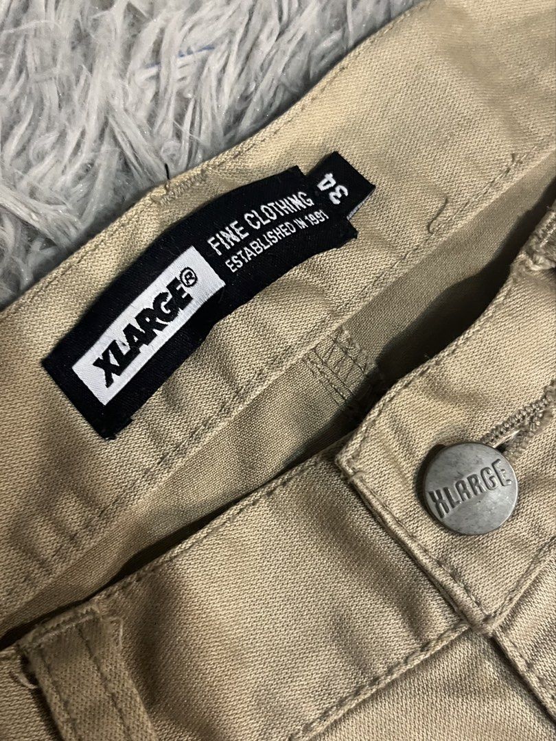 XLarge Beige Chino Pants Size 34 (Category: Chinos) located in Muntinlupa City. Submitted by pastforwardthrift (Listing ID 1470125485, Image 3). Description: - Size: XLarge (Fits waist size 34) - Color: Neutral khaki / tan - Fit: Straight leg cut - Details: Bold white branding on back waistband, logo-stamped metal button - Accent: Leather patch with gorilla graphic on back pocket - Style: Essential streetwear staple.