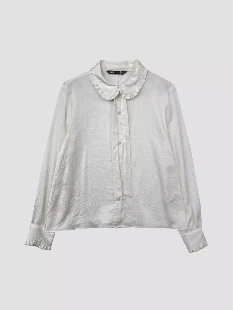 Zara White Ruffle Collar Blouse (Category: Blouses) located in Quezon City. Submitted by dropdeadprices (Listing ID 1470013046, Image 2). Description: - Brand: Zara - Condition: Brand new and never worn - Color: White - Details: Ruffle collar with neck tie string, button-up front with pearl buttons, ruffled cuffs - Fabric: Lightweight textured material.