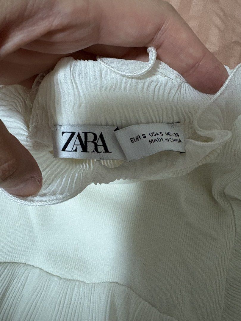 Zara White Ruffle Knit Top Size S (Category: Sleeveless) located in Quezon City. Submitted by bluefrenchorn (Listing ID 1470069350, Image 2). Description: White knit top from Zara. Size S. Features layered pleated ruffles on the shoulders and upper chest, plus pleated high collar. Ribbed texture throughout the body. Measurements: pit to pit roughly 14.5 inches, length about 15.5 inches. Fabric includes polyamide blend. Clean condition, tags attac