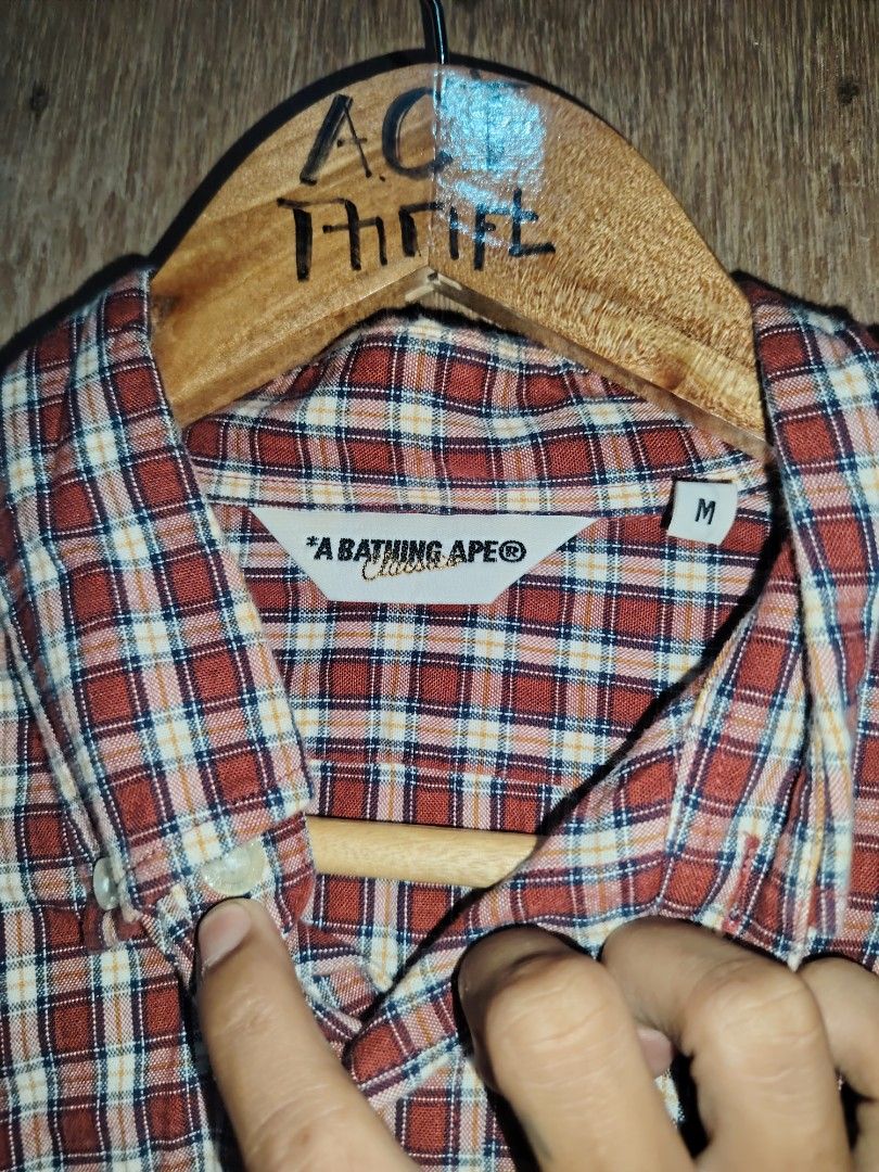 A Bathing Ape BAPE Plaid Button Down Shirt Maroon (Category: Tshirts & Polo Shirts ) located in Roxas, Palawan. Submitted by act_thrift_palawan (Listing ID 1470271779, Image 3). Description: - Brand: A Bathing Ape (BAPE) - Design: Red and white plaid button-down with long sleeves - Detail: Single chest pocket with embroidered ape head logo - Material: 100% Cotton - Origin: Made in Japan - Measurements: 21" (pit-to-pit) by 27" (length).