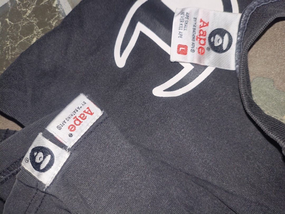 AAPE x Champion Collaboration T-Shirt (Category: Tshirts & Polo Shirts ) located in Narvacan. Submitted by picky_looter (Listing ID 1470298238, Image 3). Description: - Brand: AAPE by A Bathing Ape x Champion - Size: L (tagged at collar and sleeve) - Color: Black - Details: Front ape head and Champion chest logos, sleeve text print - Back: Distinctive camo pattern panel with large typography prints - Mode of Payment: BPI, GCash, or COD via LBC - 