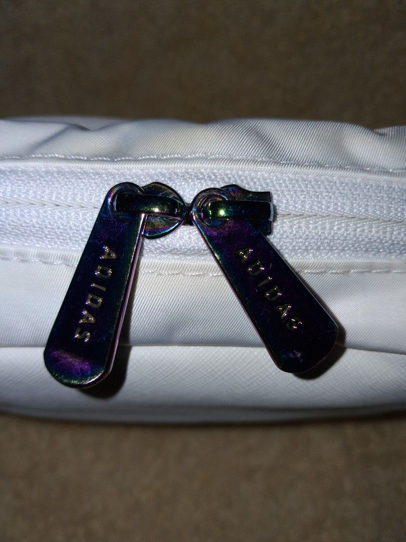 Adidas White Toiletry Bag Pouch With 3 Stripes (Category: Belt bags, Clutches and Pouches) located in Angeles City. Submitted by anneps (Listing ID 1470219127, Image 2). Description: - Brand: Adidas - Color: White with iconic 3 black stripes - Features: Side carry handle and unique rainbow metallic-tinted logo zipper pulls - Interior: Light pink lining with a convenient mesh slip pocket - Dimensions: Approximately 8 inches tall - Perfect for: Tra