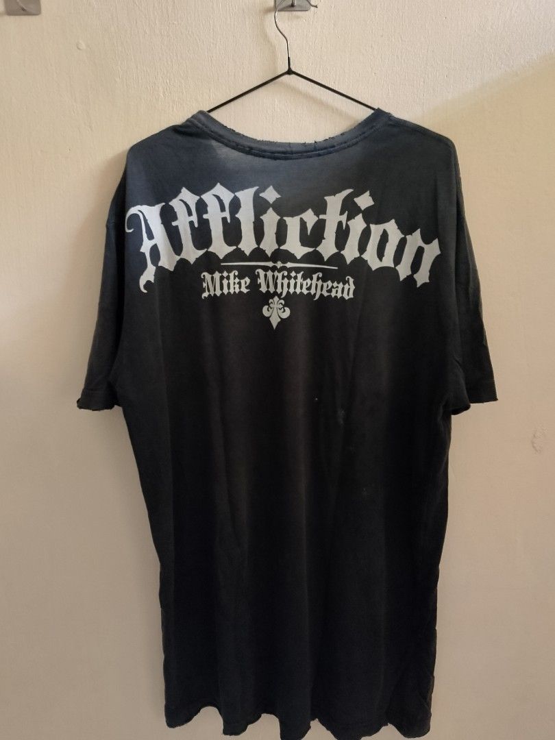 Affliction Mike Whitehead Skull Graphic T-Shirt (Category: Tshirts & Polo Shirts ) located in Caloocan City. Submitted by ricecell (Listing ID 1470295416, Image 2). Description: - Brand: Affliction - Design: Dual skull and helmet graphic with gothic lettering and Mike Whitehead back signature - Color: Dark charcoal wash with natural fading - Fit: Relaxed, short sleeves - Details: Distressed collar and sleeve edges for a worn-in look - Material: S