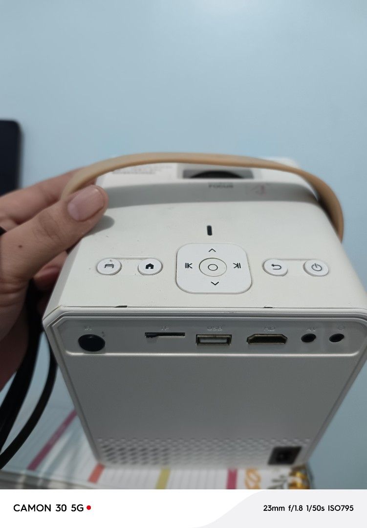 Android TV Portable Smart Projector Wi-Fi Bluetooth (Category: Projectors) located in Manila. Submitted by cleverearth.ed94b6 (Listing ID 1470248302, Image 2). Description: - Portable smart projector in a sleek white cube design - Features a stylish brown carrying handle for easy travel - Decorated with a cute pink 'Read More Books' sticker - Equipped with HDMI, USB, and TF card slots - Perfect for cozy movie nights anywhere, anytime - PM for qui