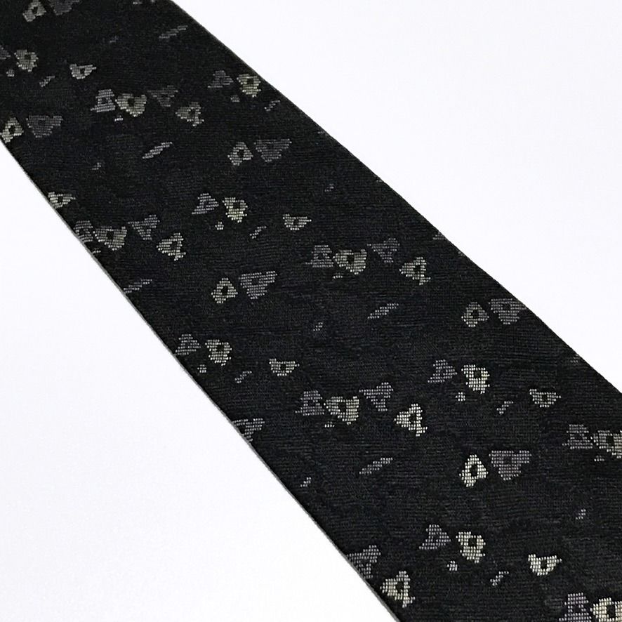 AXUM Vintage Abstract Black Neck Tie (Category: Ties) located in Taguig. Submitted by retrogaze (Listing ID 1470210817, Image 3). Description: This vintage 100% silk necktie by AXUM Men features a solid black ground woven with a subtle, slubbed texture that lends refined tactile depth to the fabric. The body is decorated with an understated abstract geometric pattern of scattered, pixelated micro-shapes woven in soft cream, taupe, and muted slate