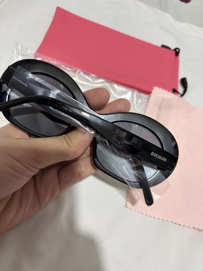 Baobab Black Oval Sunglasses (Category: Sunglasses & Eyewear) located in Valenzuela. Submitted by cheaper_finds (Listing ID 1470152874, Image 2). Description: - Brand: Baobab - Style: Black oval sunglasses with thick frames and dark lenses - Details: Branded temples with 'Baobab' and 'See differently' text - Inclusions: Bright pink drawstring pouch, light pink microfiber cleaning cloth, and protective plastic wrapping - Condition: Brand new / pri