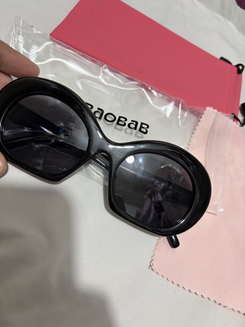 Baobab Black Oval Sunglasses (Category: Sunglasses & Eyewear) located in Valenzuela. Submitted by cheaper_finds (Listing ID 1470152874, Image 1). Description: - Brand: Baobab - Style: Black oval sunglasses with thick frames and dark lenses - Details: Branded temples with 'Baobab' and 'See differently' text - Inclusions: Bright pink drawstring pouch, light pink microfiber cleaning cloth, and protective plastic wrapping - Condition: Brand new / pri