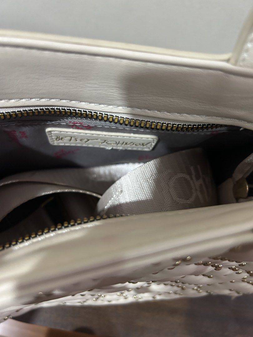 Betsey Johnson Off-White Structured Handbag with Branded Strap (Category: Luxury Bags & Wallets) located in Marilao. Submitted by bamito (Listing ID 1470166884, Image 3). Description: - Color: Off-white with gold-tone hardware - Style: Structured handbag / top-handle bag - Closure: Secure top zip - Straps: Double top handles + wide removable canvas shoulder strap with repeating text pattern.