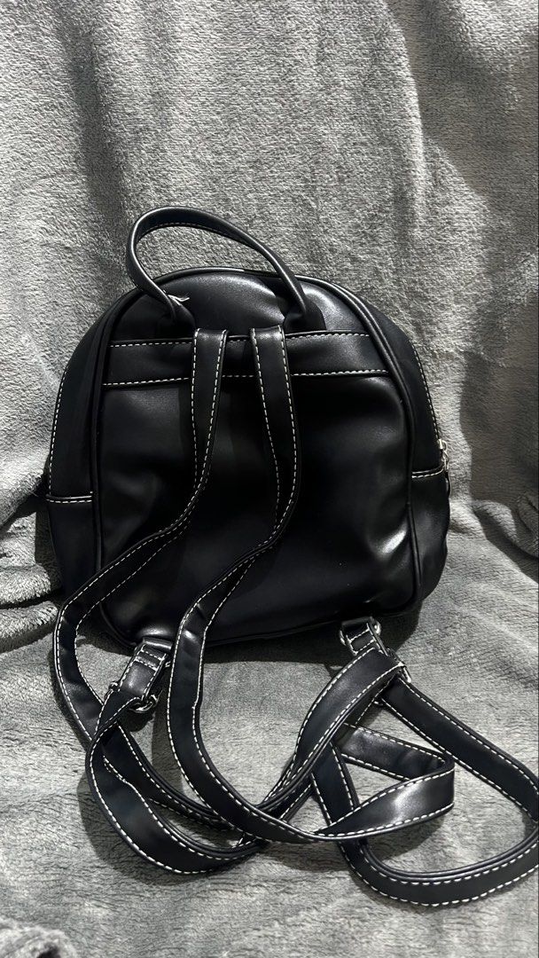 Black leather mini backpack (Category: Backpacks) located in Manila. Submitted by asdfghjkl.mountain (Listing ID 1470278269, Image 2). Description: - Color & Material: Black faux leather - Design: White contrast stitching along seams and straps - Storage: Front zipped pocket with round silver puller - Carry Options: Adjustable shoulder straps and top carry handle - Size: Small everyday mini backpack.